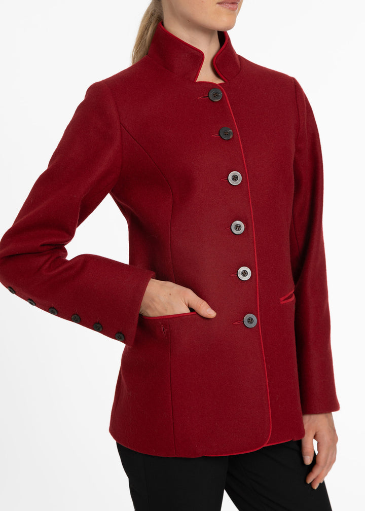 A woman wearing a structured, long-sleeved red jacket with a high stand collar and dark buttons, shown from the neck down against a plain white background.