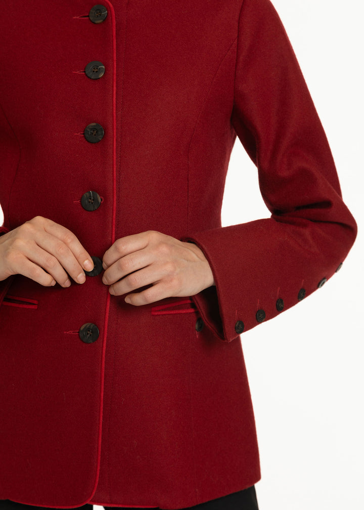 A close-up of a person wearing a deep red wool-blend jacket with black buttons, showing the hands adjusting the front closure against a plain white background.