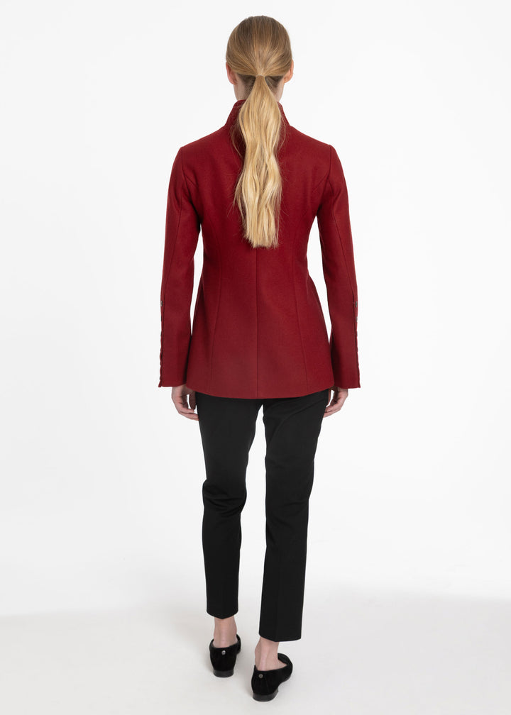 A woman viewed from the back wearing a structured dark red jacket, black pants, and black flats against a plain white studio background.