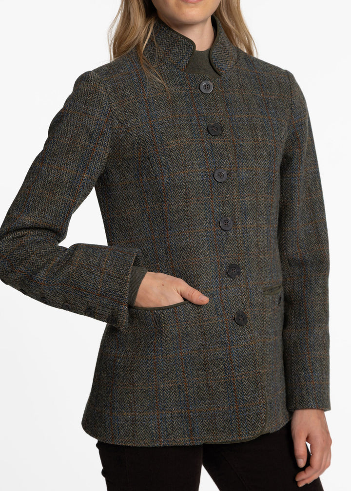 A woman wearing a dark green and tweed jacket with a subtle plaid pattern, featuring a high stand collar and dark buttons, shown against a plain white background.