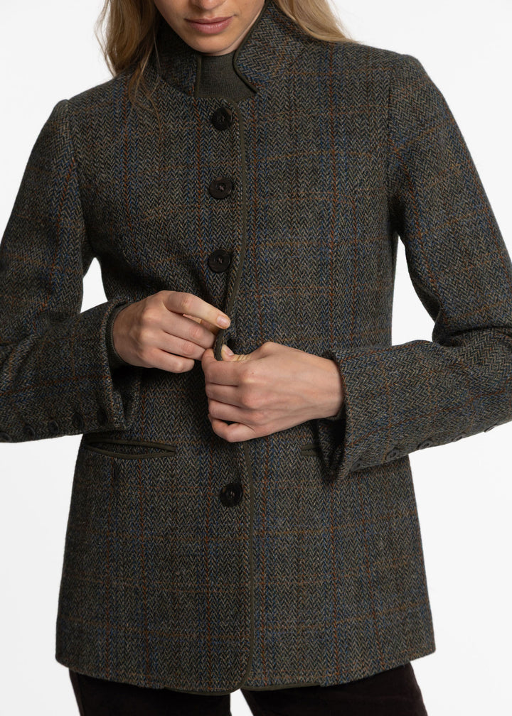 Close up image of a woman wearing a green plaid herringbone jacket with dark brown buttons down the front.