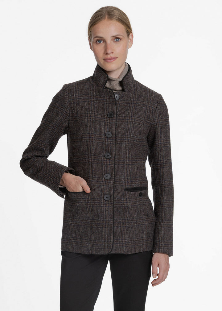 A woman modeling a dark brown and black checkered jacket with a high stand collar, front buttons, and a high-waisted silhouette, paired with black trousers against a plain white background.