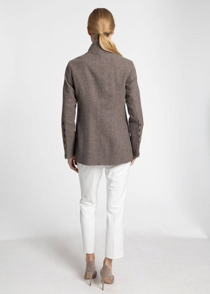 A woman shown from the back wearing a grey herringbone jacket, white trousers, and beige heels against a plain white studio background.