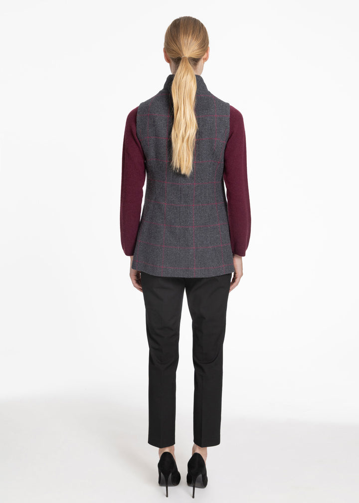 A woman viewed from the back wearing a sleeveless gray plaid waistcoat over a burgundy long-sleeve top, black trousers, and black heels against a plain white studio background.