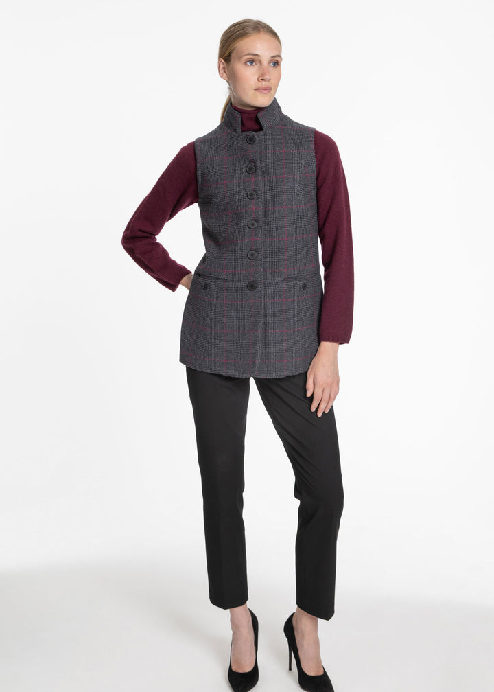 A woman modeling a gray and black plaid wool waistcoat over a burgundy long-sleeve top, paired with black trousers and black heels, against a plain white studio background.