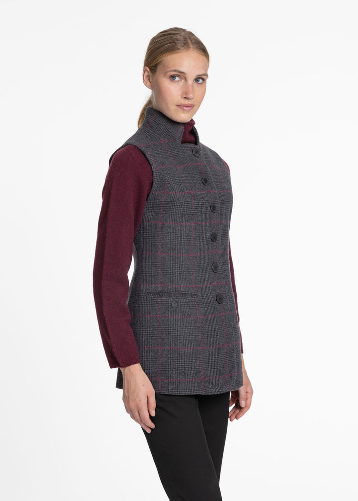 A woman modeling a sleeveless dark gray and black checkered waistcoat over a burgundy long-sleeve shirt and black pants, photographed against a plain white studio background.