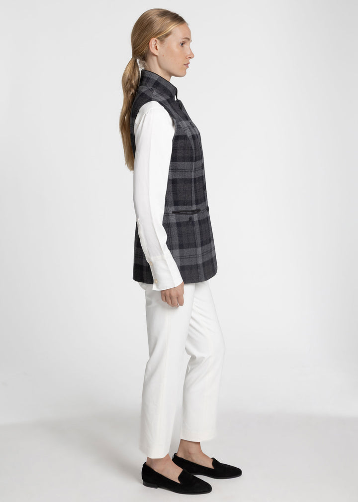 Side view of a woman wearing a black and grey wool waistcoat with a white sweater and white trousers. 