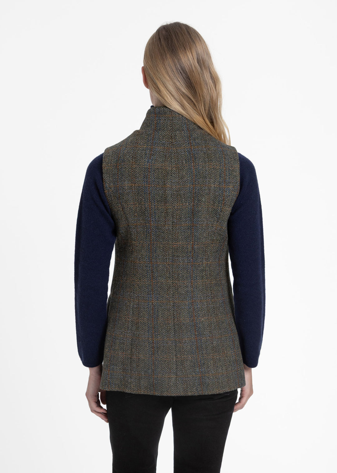 A woman shown from the back wearing a green tweed waistcoat over a navy blue long-sleeve top and black pants, against a plain white studio background.