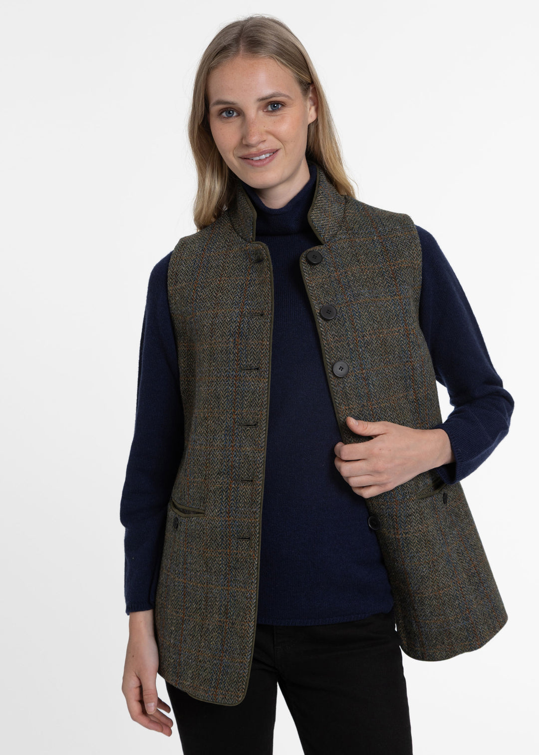 Woman wearing a green check wool waistcoat paired with a navy knit sweater. 