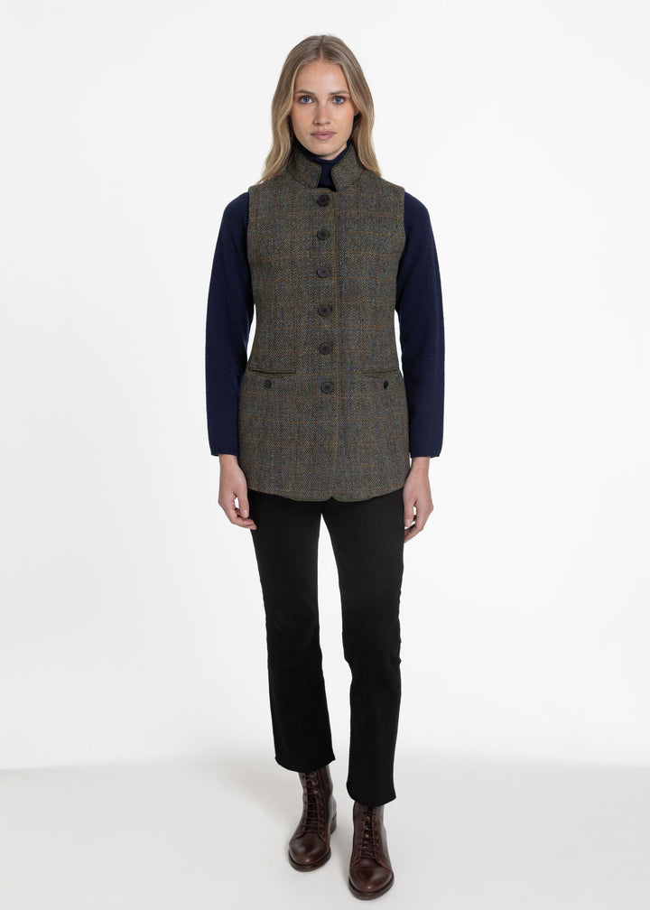 Woman wearing a green check wool waistcoat paired with a navy knit sweater and cropped black trousers against a white background.