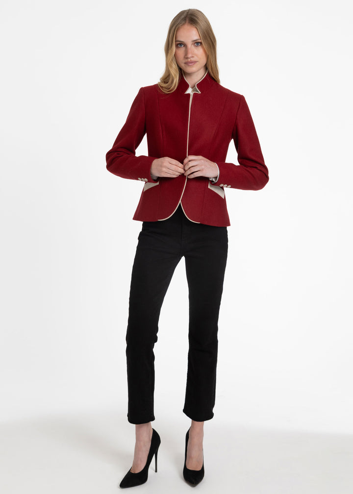 A woman modeling a structured, red blazer with a high stand collar paired with black cropped trousers and black heels, against a plain white studio background.