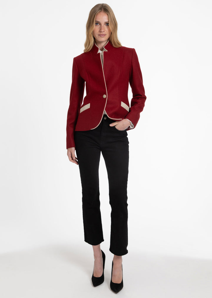 Woman wearing a red tailored jacket with beige trim and pocket flaps on a white background.
