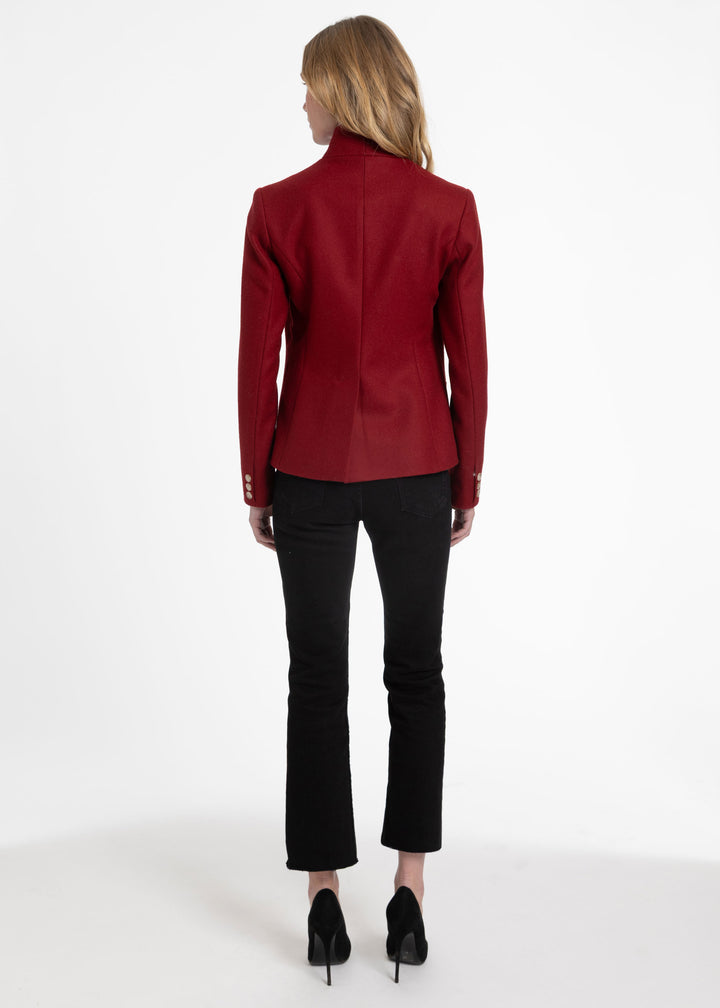 A woman viewed from the back wearing a structured red blazer, black cropped pants, and black heels against a plain white studio background.