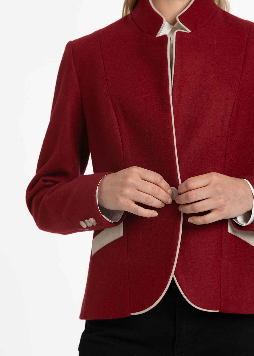 A close-up of a model wearing a structured red blazer with cream-colored piping and a high stand collar, buttoned at the front.