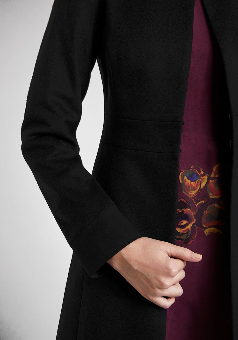 A model wears the Buxton coat in black wool cashmere, an elegant occasionwear style featuring a standing collar and deep suede cuffs.