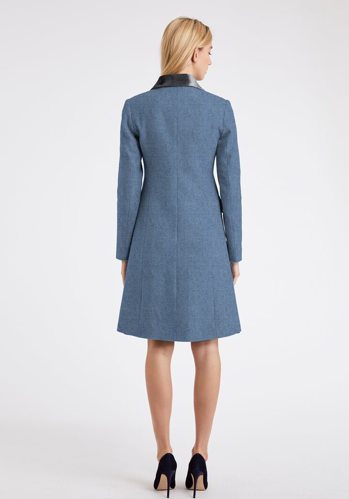 The back of a woman wearing a blue coat with a grey velvet collar trim on a white background