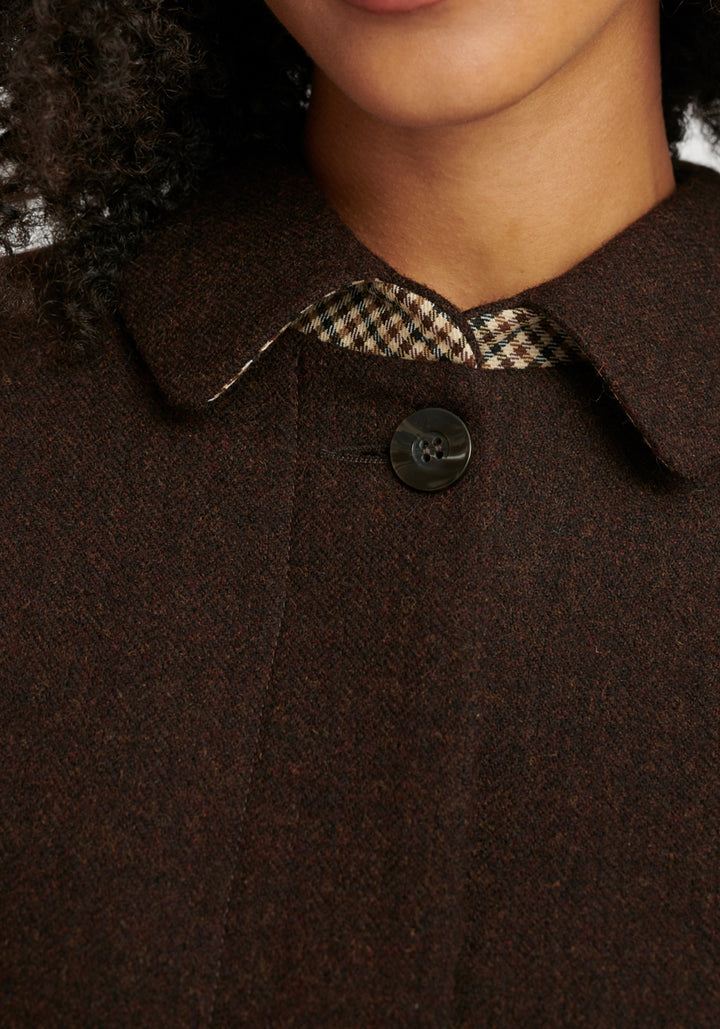 Close-up of a brown coat with a button and checkered under collar detail.