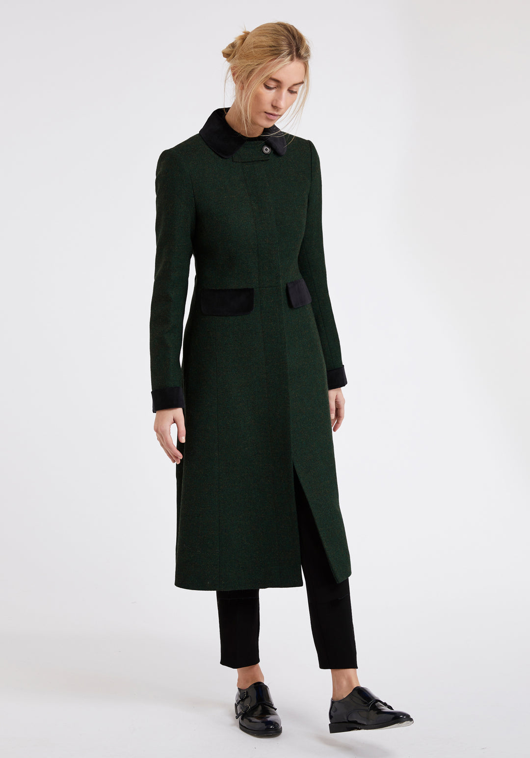 Woman wearing a green wool coat with black detailing around the collar, pocket flaps, and cuffs
