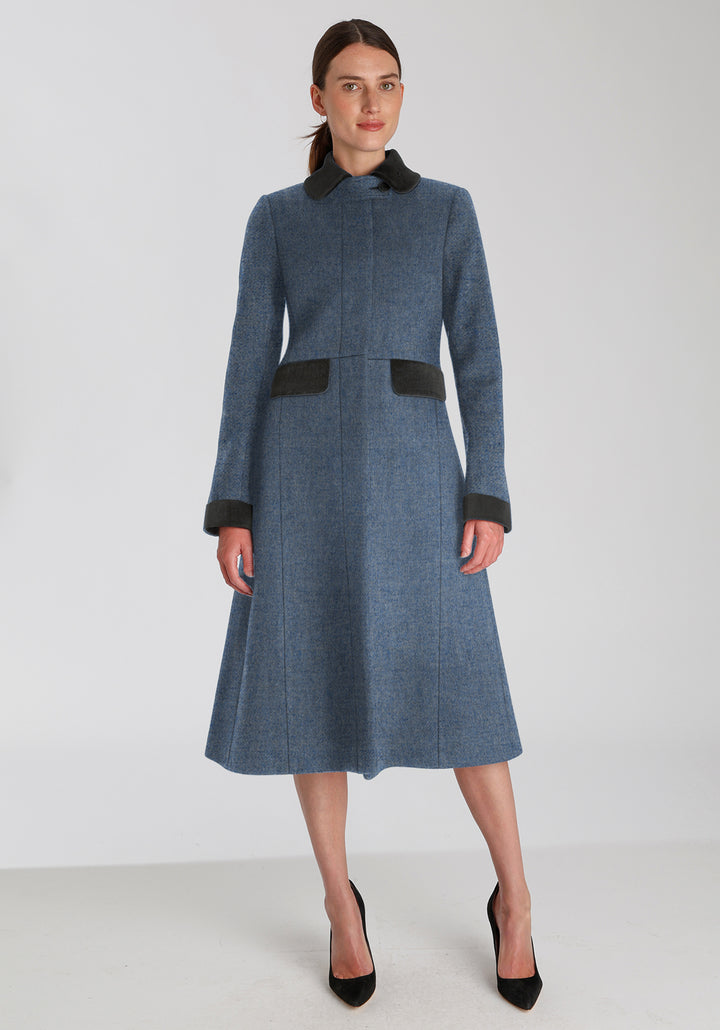 Woman wearing blue wool coat with dark grey pocket, collar, and cuff detailing 
