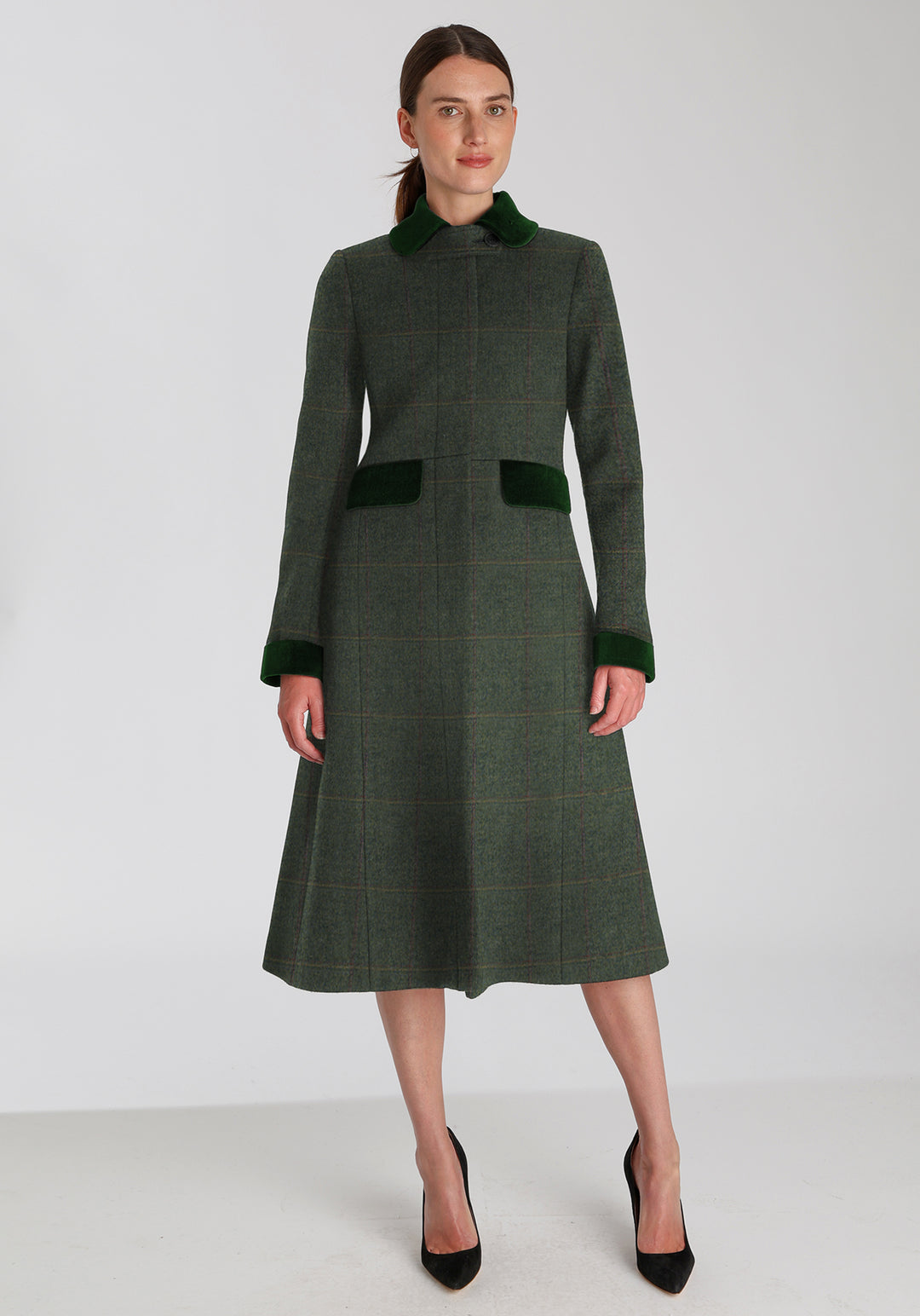 Woman wearing sage green wool coat with a faint yellow and red overcheck. Dark green detailing on the collar, cuffs, and pocket flaps