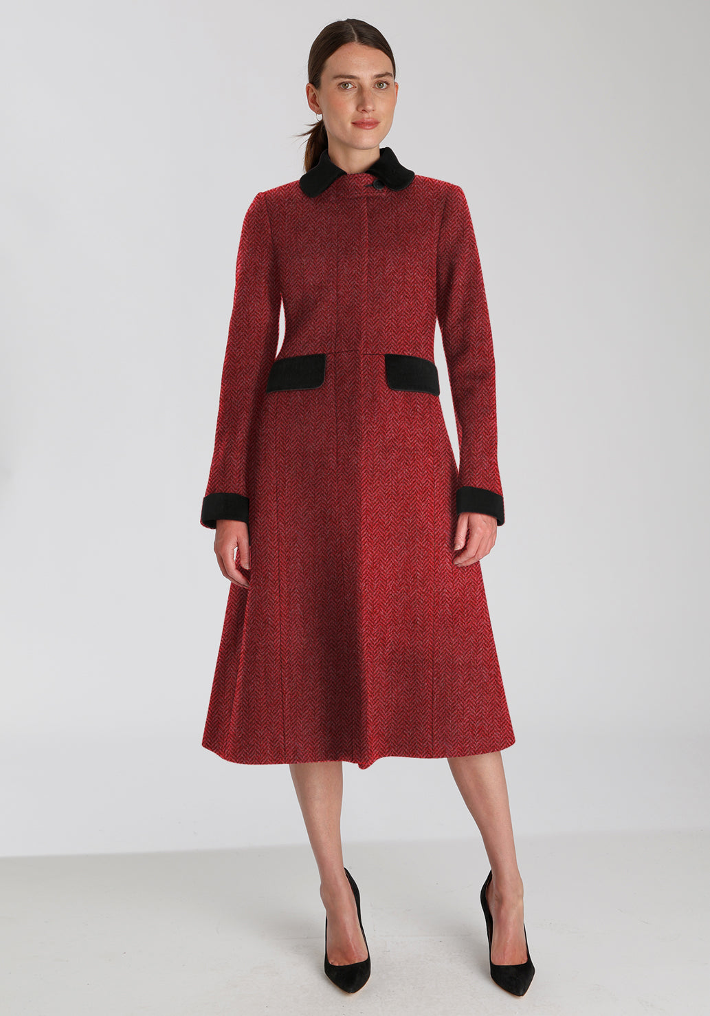 Woman wearing red and pink herringbone coat with black detailing on the collar, cuffs, and pocket flaps