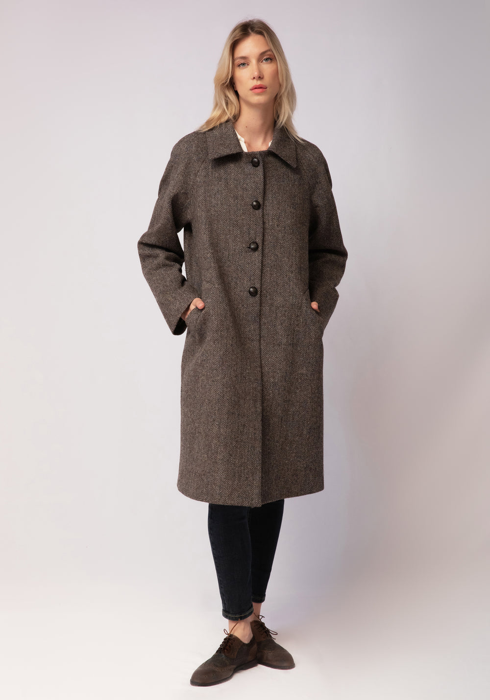 A model wears the Dari coat, featuring a relaxed cocoon silhouette and classic raglan sleeves in a heather Harris Tweed herringbone.