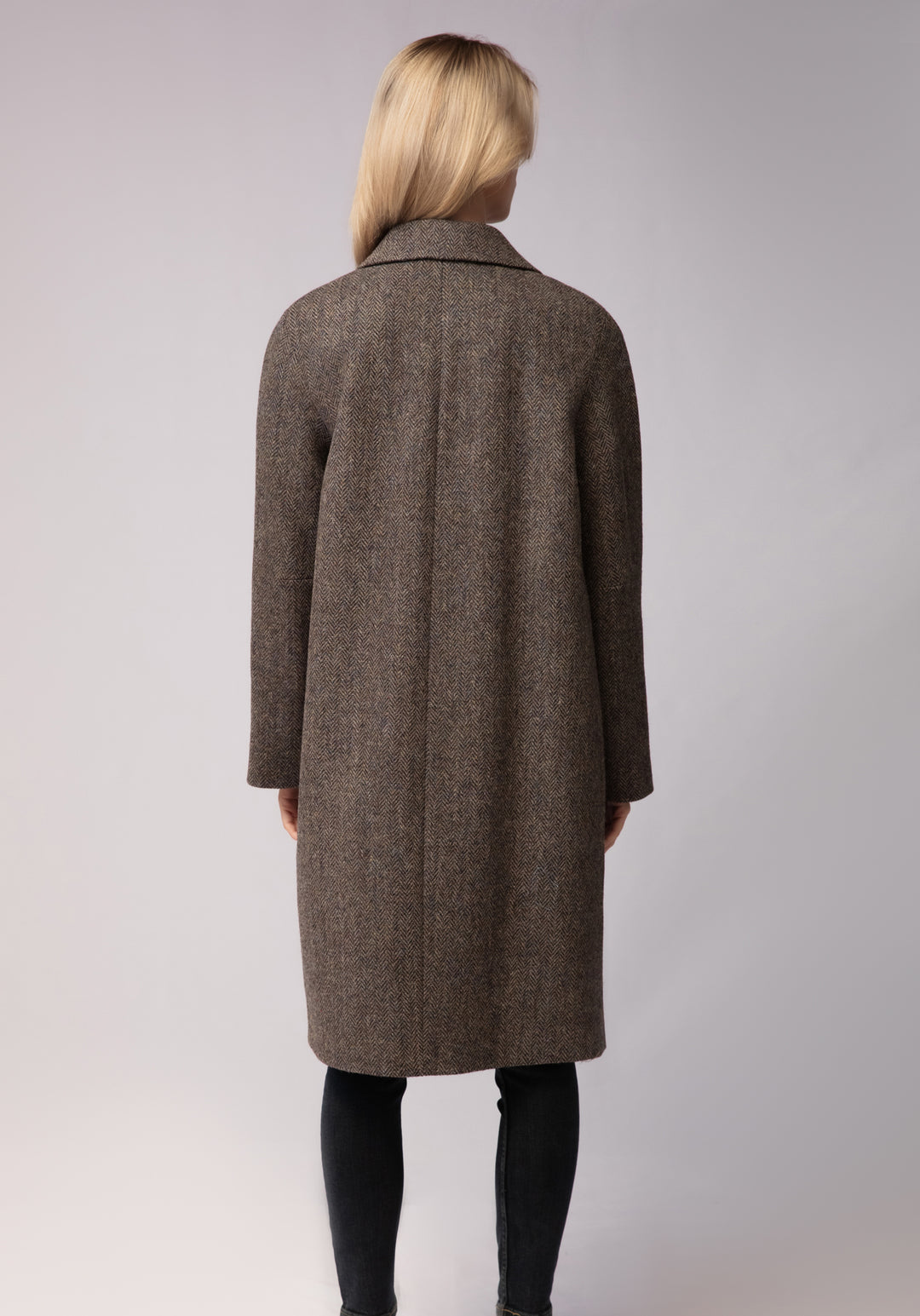 A model wears the Dari coat, featuring a relaxed cocoon silhouette and classic raglan sleeves in a heather Harris Tweed herringbone.