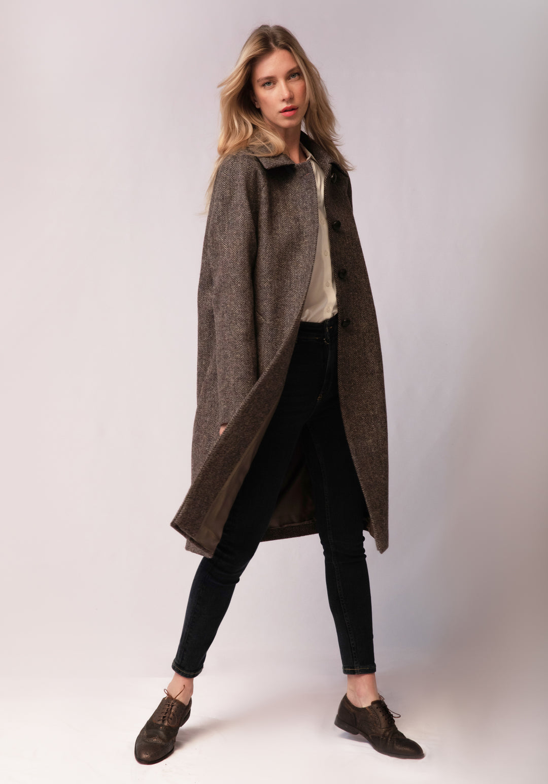 A model wears the Dari coat, featuring a relaxed cocoon silhouette and classic raglan sleeves in a heather Harris Tweed herringbone.