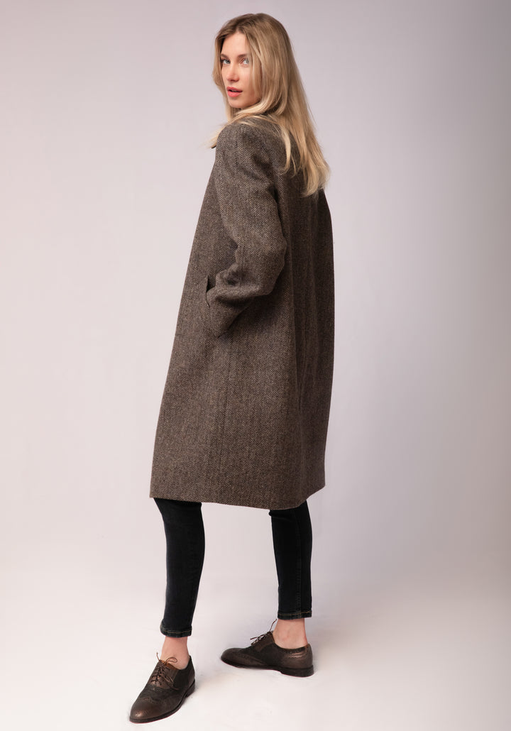 A model wears the Dari coat, featuring a relaxed cocoon silhouette and classic raglan sleeves in a heather Harris Tweed herringbone.