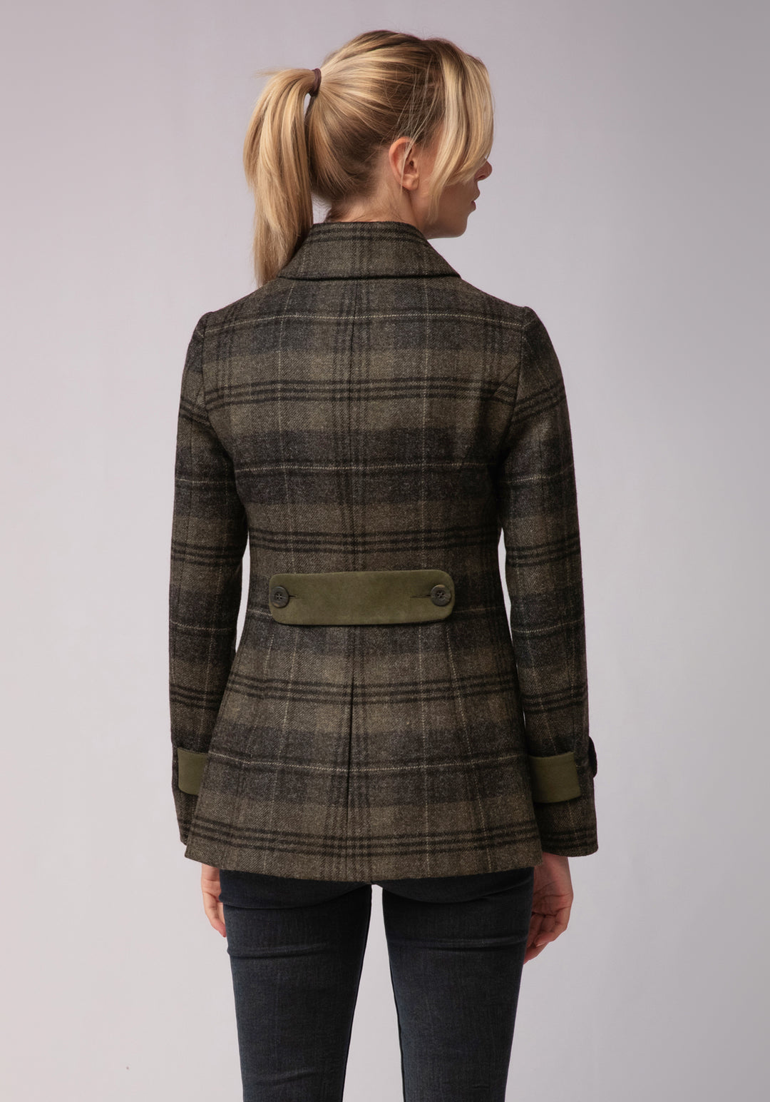 Back of woman wearing grey and green check wool jacket with moss green cuff and back belt detail