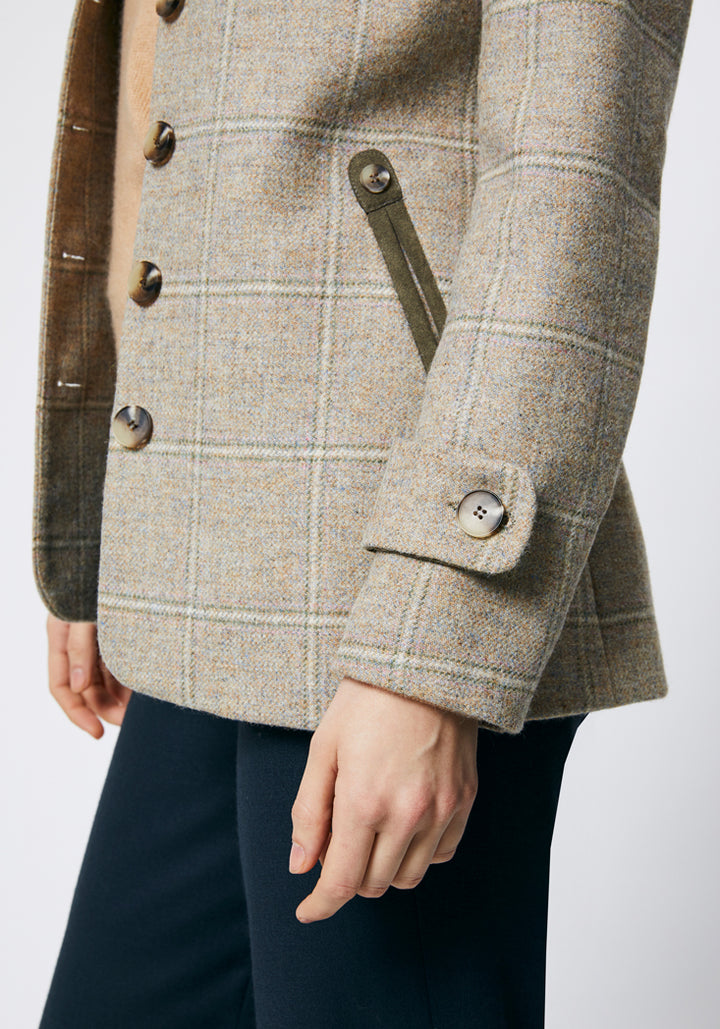 Close up on the side of a cream check jacket with cuff detailing ang moss green trim around the pockets