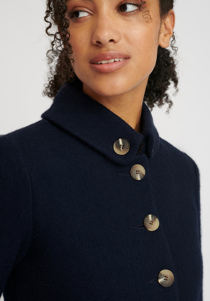 A model wears the Hendre jacket in navy, a structured, slim-fit design with high collar and suede trim.