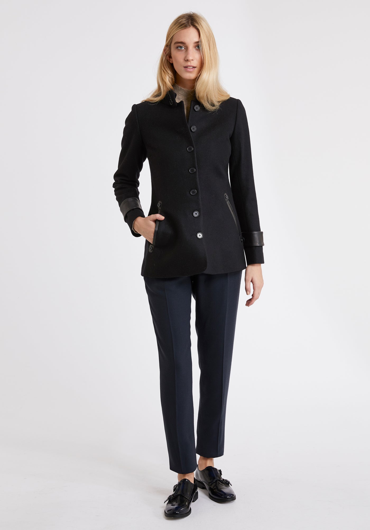 A model wears the Hendre jacket in black, a structured, slim-fit design with high collar and suede trim.