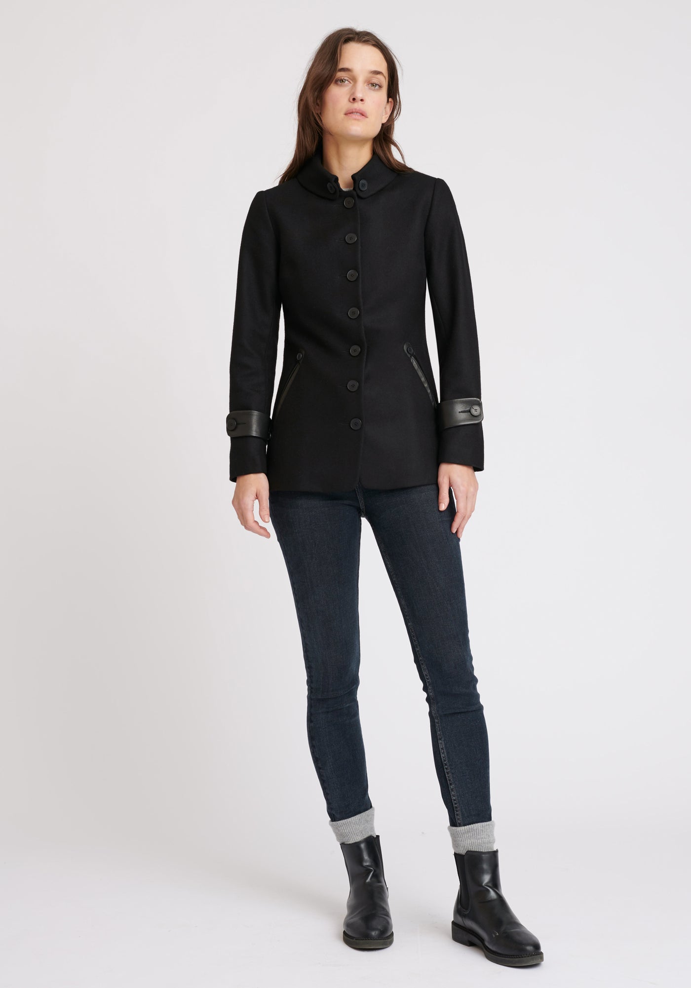 A model wears the Hendre jacket in black, a structured, slim-fit design with high collar and suede trim.