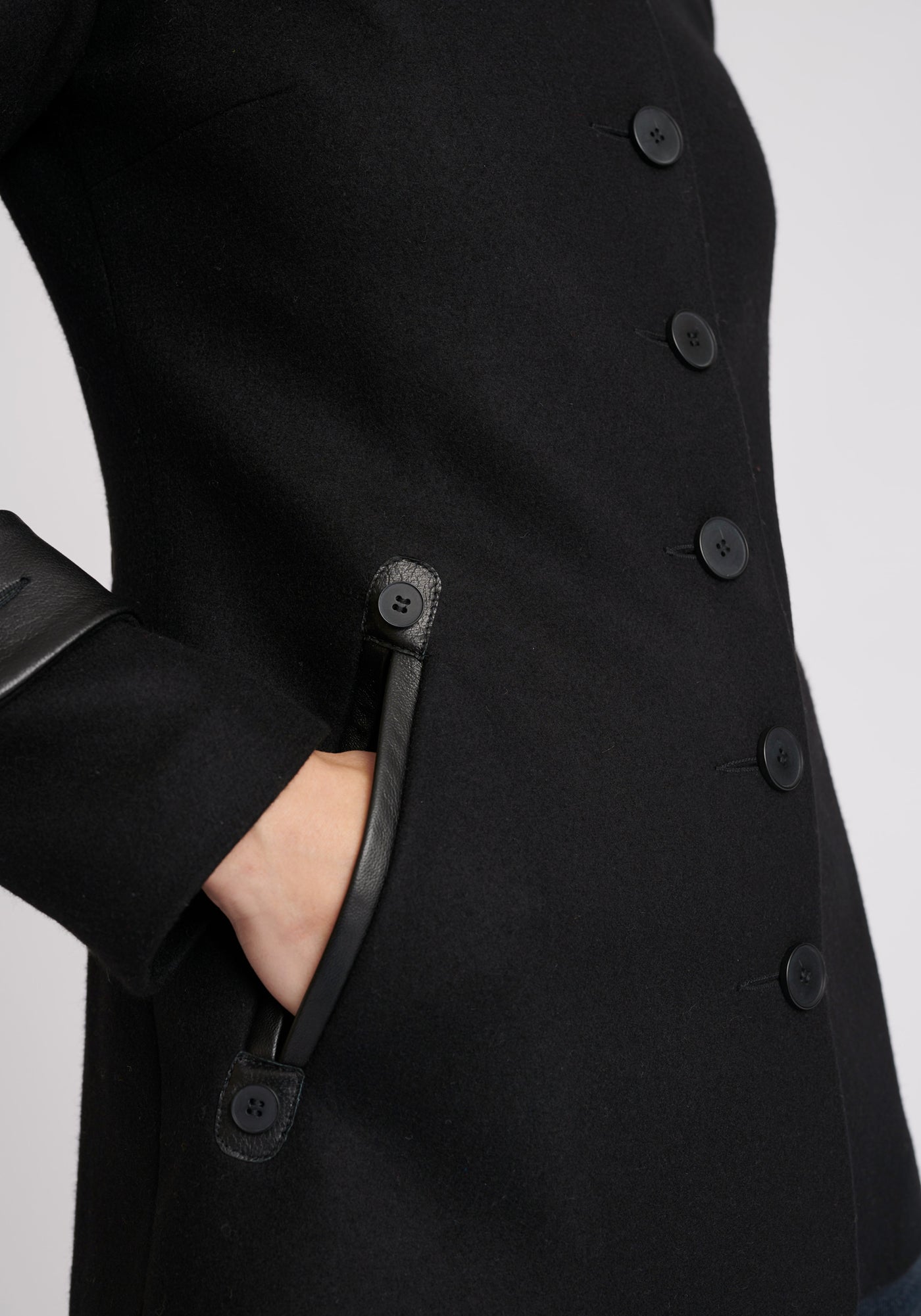 A model wears the Hendre jacket in black, a structured, slim-fit design with high collar and suede trim.