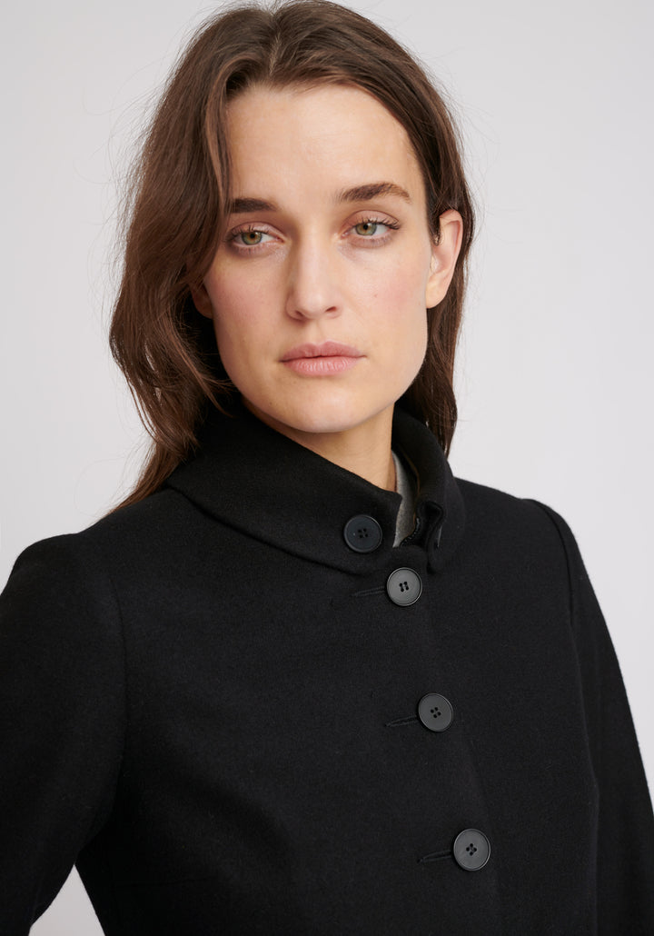 A model wears the Hendre jacket in black, a structured, slim-fit design with high collar and suede trim.