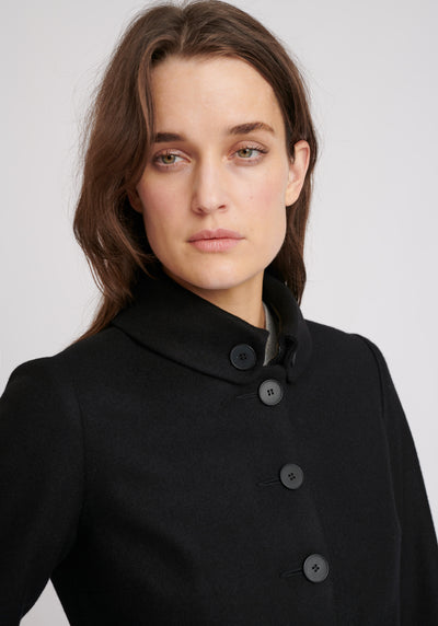 A model wears the Hendre jacket in black, a structured, slim-fit design with high collar and suede trim.