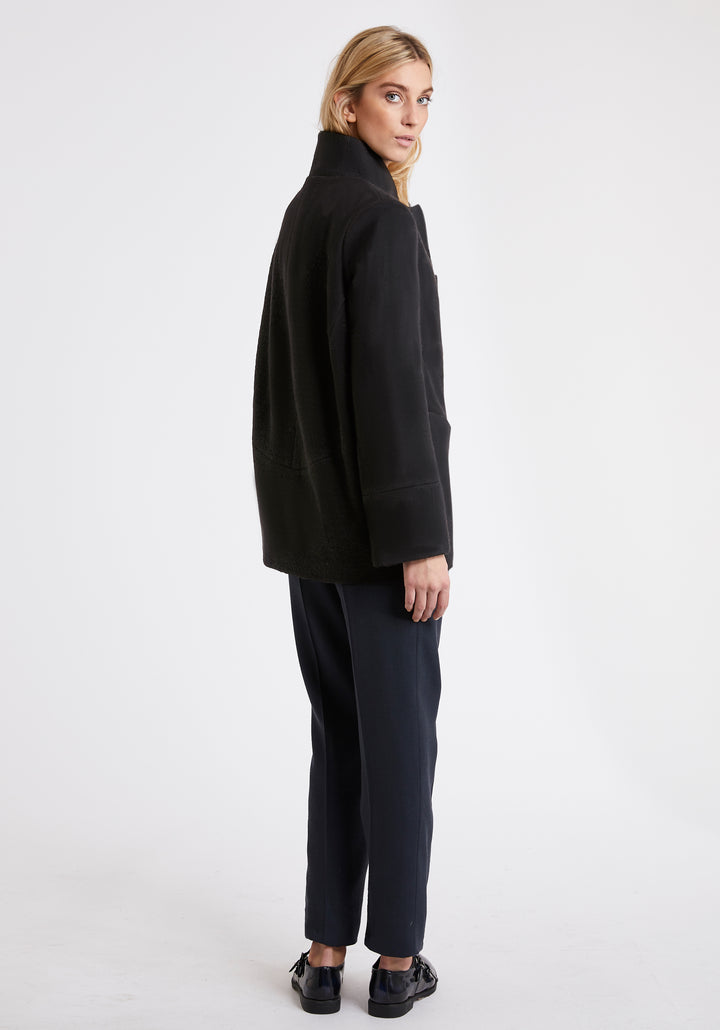  A model wears the Jackson jacket in black, a structured piece with unique cut-out standing collar and deep panelling on the body and cuffs.