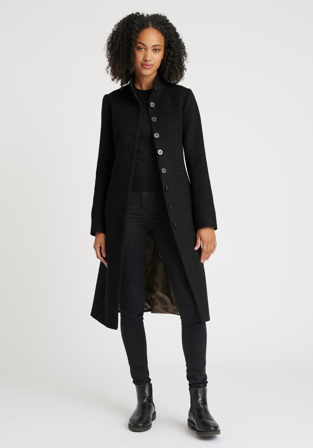 A model wears the Opera coat, a fitted, longline coat made from Italian black wool cashmere, finished with black suede trim.