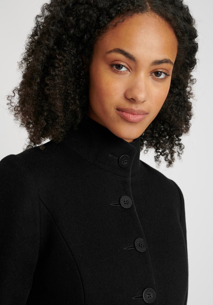 A model wears the Opera coat, a fitted, longline coat made from Italian black wool cashmere, finished with black suede trim.