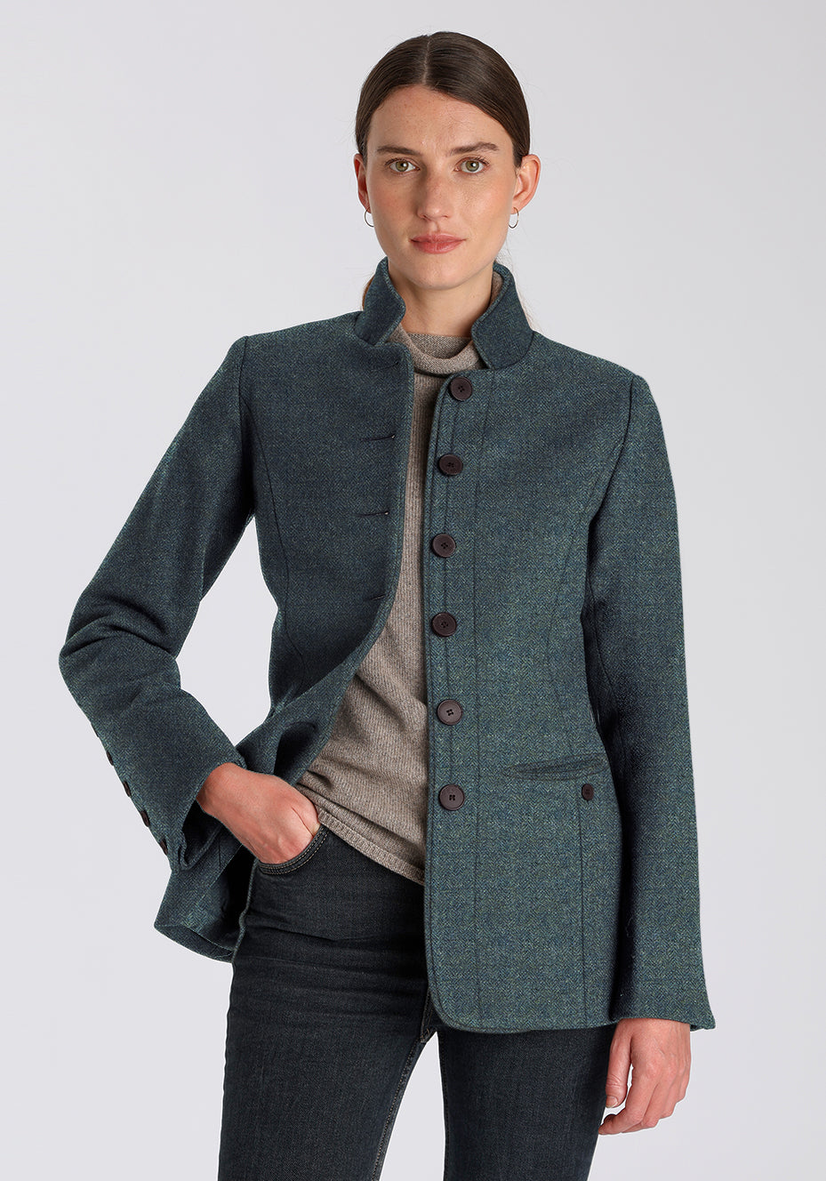 Woman wearing a teal wool jacket with brown buttons down the front on a plain background