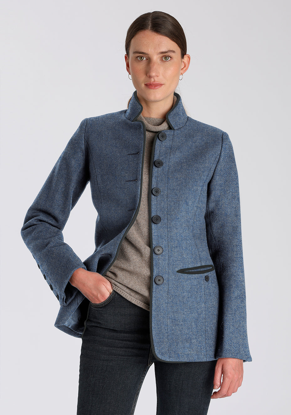 Woman wearing a blue jacket with slate grey buttons down the front on a plain background