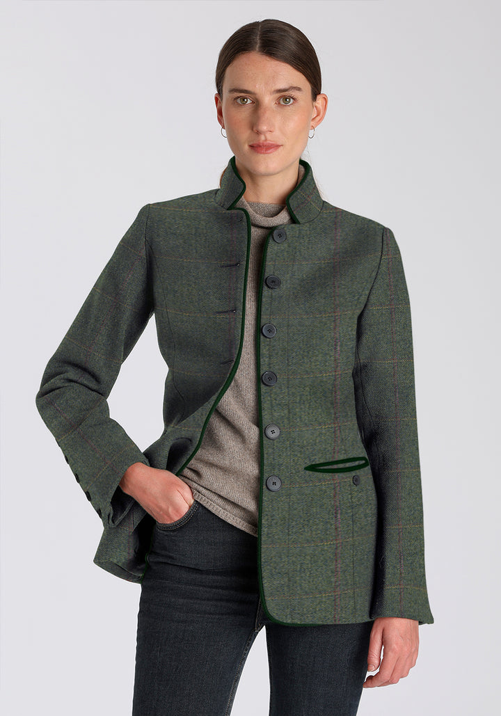 Woman wearing a green wool jacket with a yellow and red check and green trim on a plain background