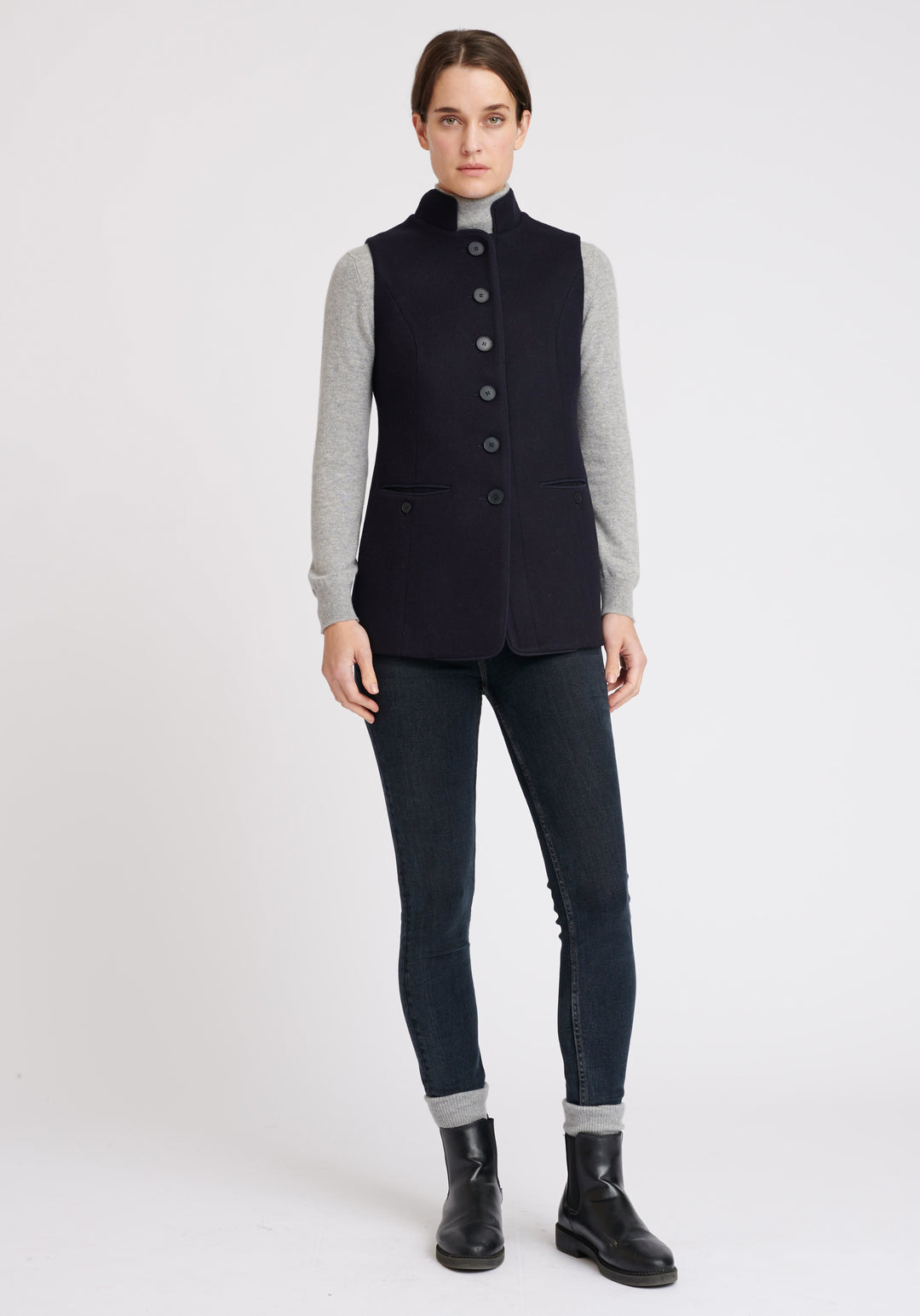 A model wears the Patmos waistcoat in navy, a hip-length style with mandarin collar and front pocket detailing finished with tonal suede trim.