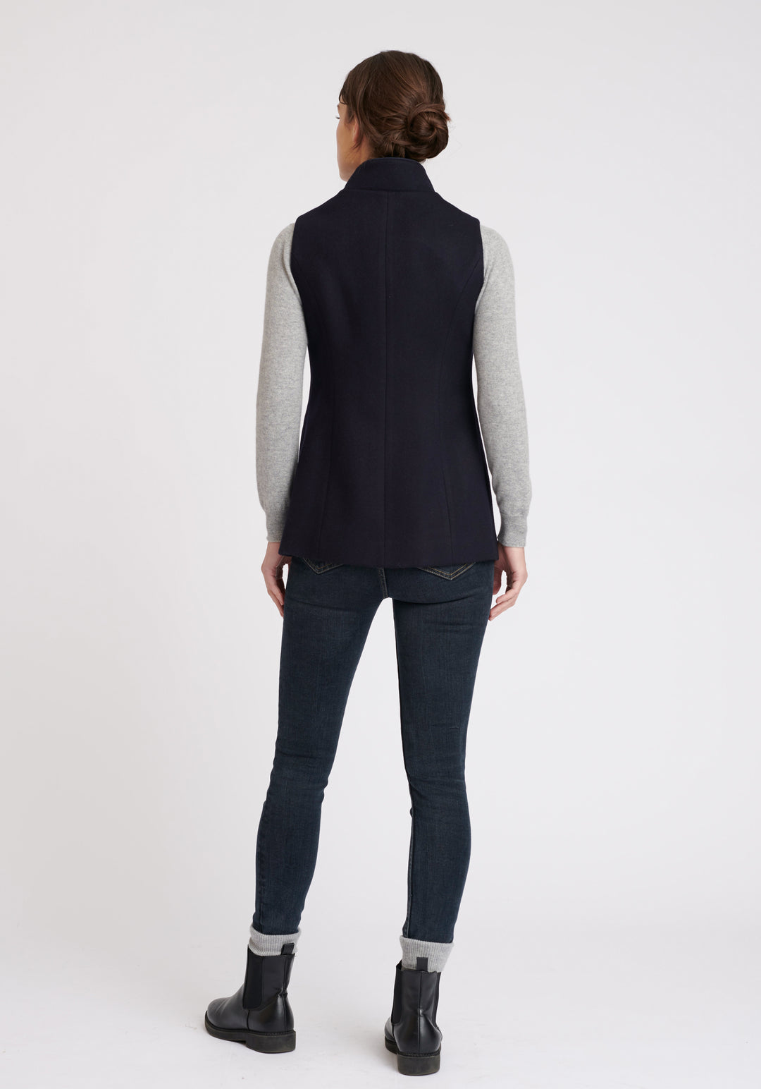A model wears the Patmos waistcoat in navy, a hip-length style with mandarin collar and front pocket detailing finished with tonal suede trim.