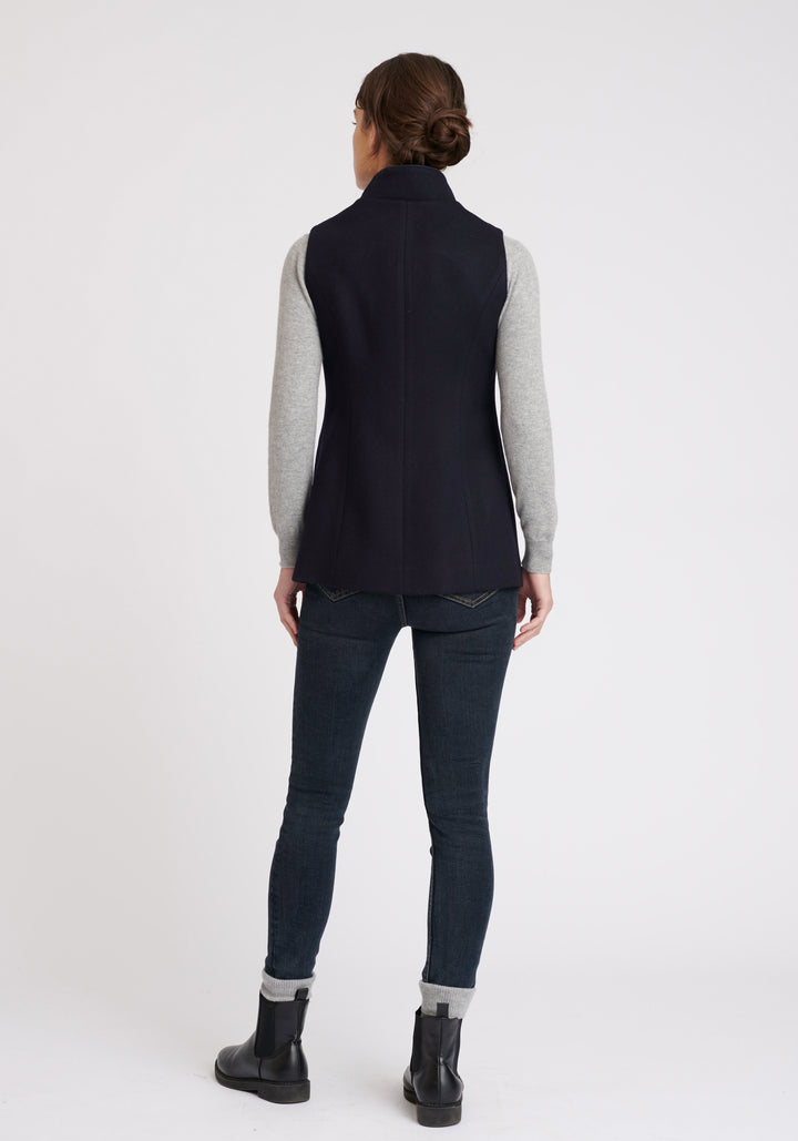 A model wears the Patmos waistcoat in navy, a hip-length style with mandarin collar and front pocket detailing finished with tonal suede trim.