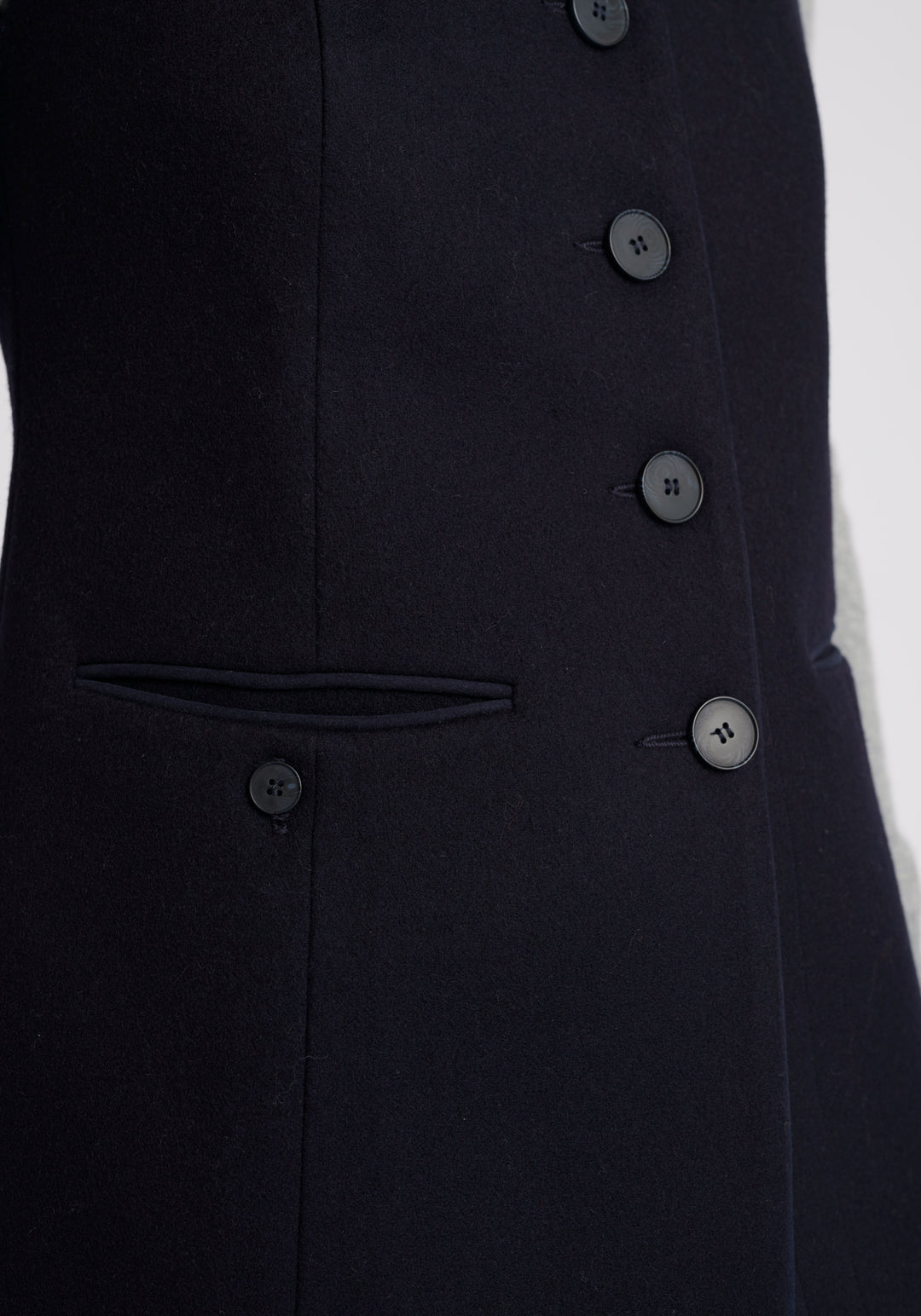A model wears the Patmos waistcoat in navy, a hip-length style with mandarin collar and front pocket detailing finished with tonal suede trim.