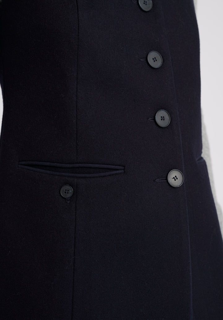 A model wears the Patmos waistcoat in navy, a hip-length style with mandarin collar and front pocket detailing finished with tonal suede trim.