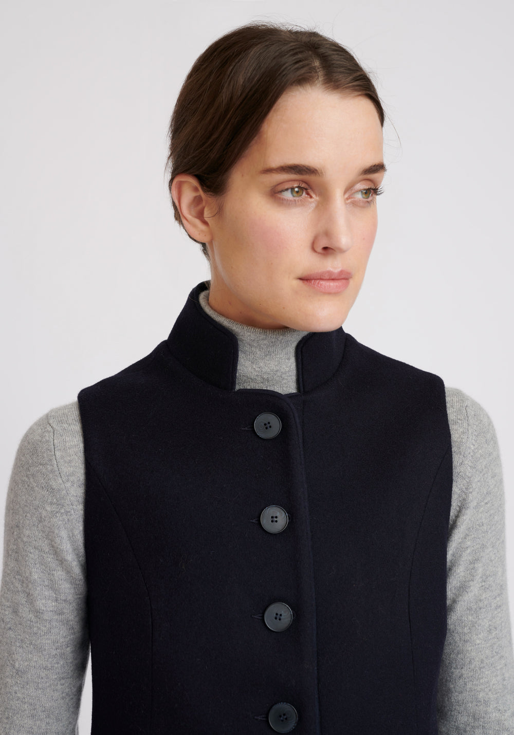 A model wears the Patmos waistcoat in navy, a hip-length style with mandarin collar and front pocket detailing finished with tonal suede trim.