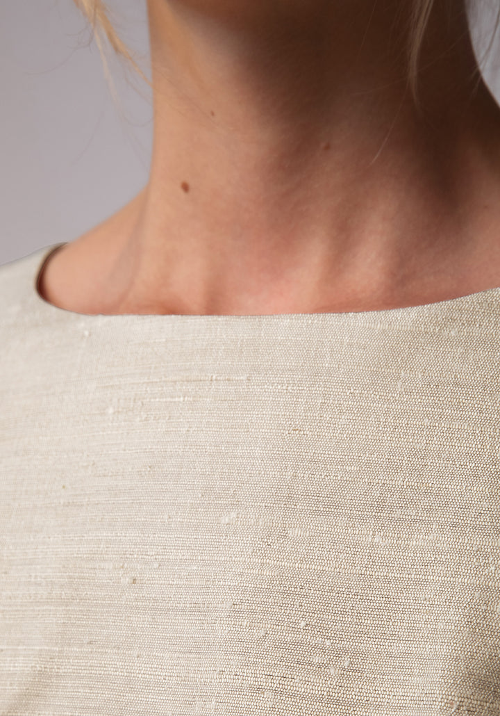 Close-up of a person wearing a beige textured dress with a neutral background